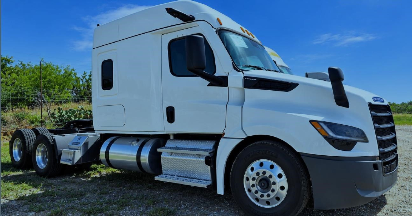 Truck cab showing Freightliner Cascadia 126 in-service area with white exterior and side fuel tanks, front grille, and door windows.