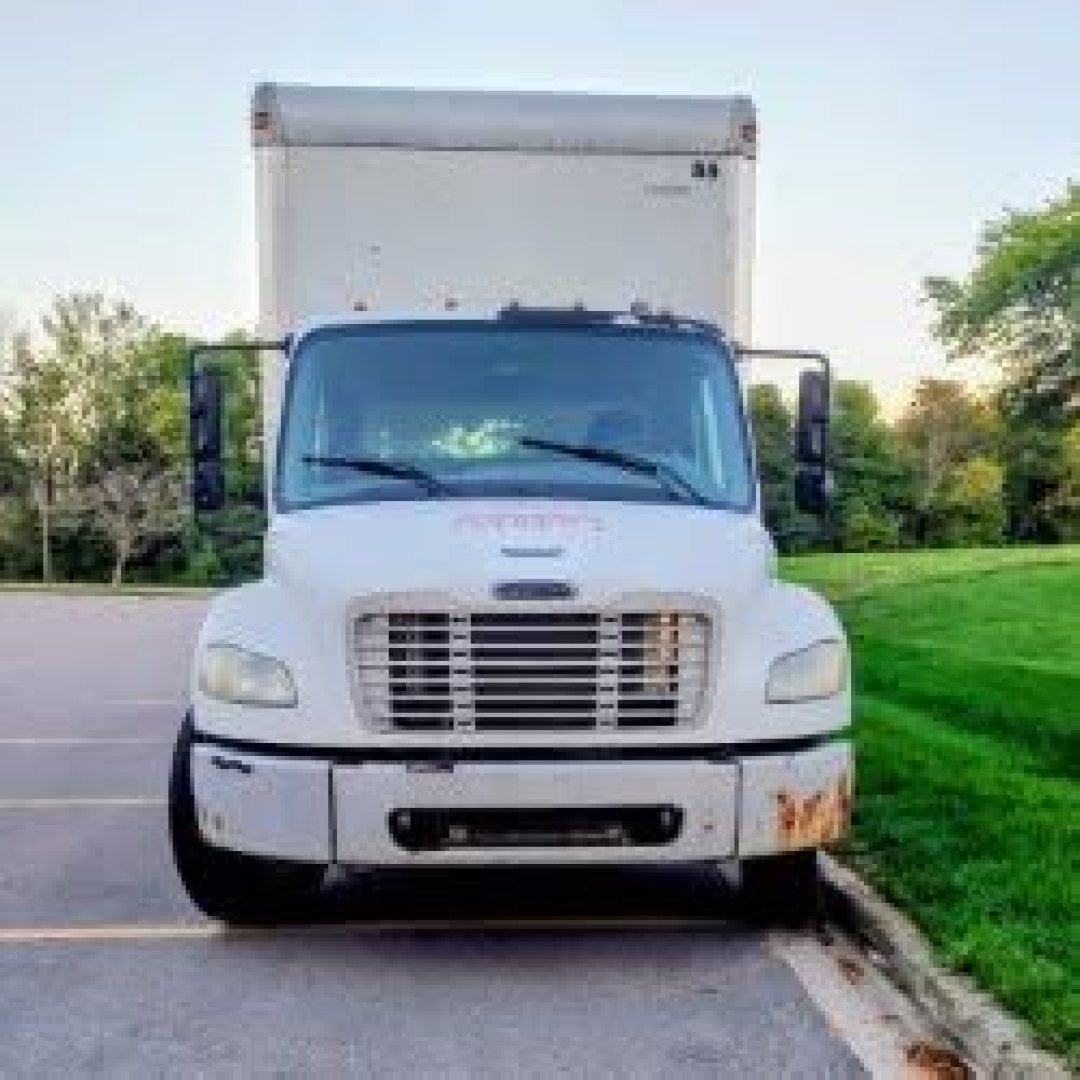 White Freightliner M2 106 box truck front view with grille, headlights, and bumper; windshield wipers and side mirrors visible.