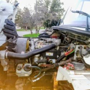 Engine bay of a Freightliner M2 106 truck showing hoses, wiring, and engine components.