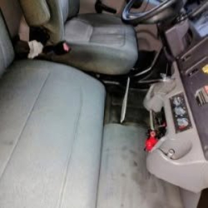 Interior of a Freightliner M2 106 cab showing front seats and dashboard with steering column and floor area.