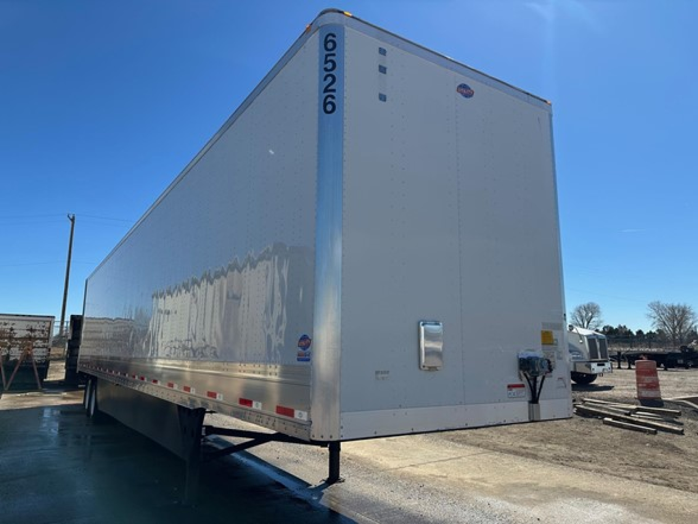 Utility trailer showing a 65-526 vertical numbers on the front corner and rear doors with a reflective white exterior.