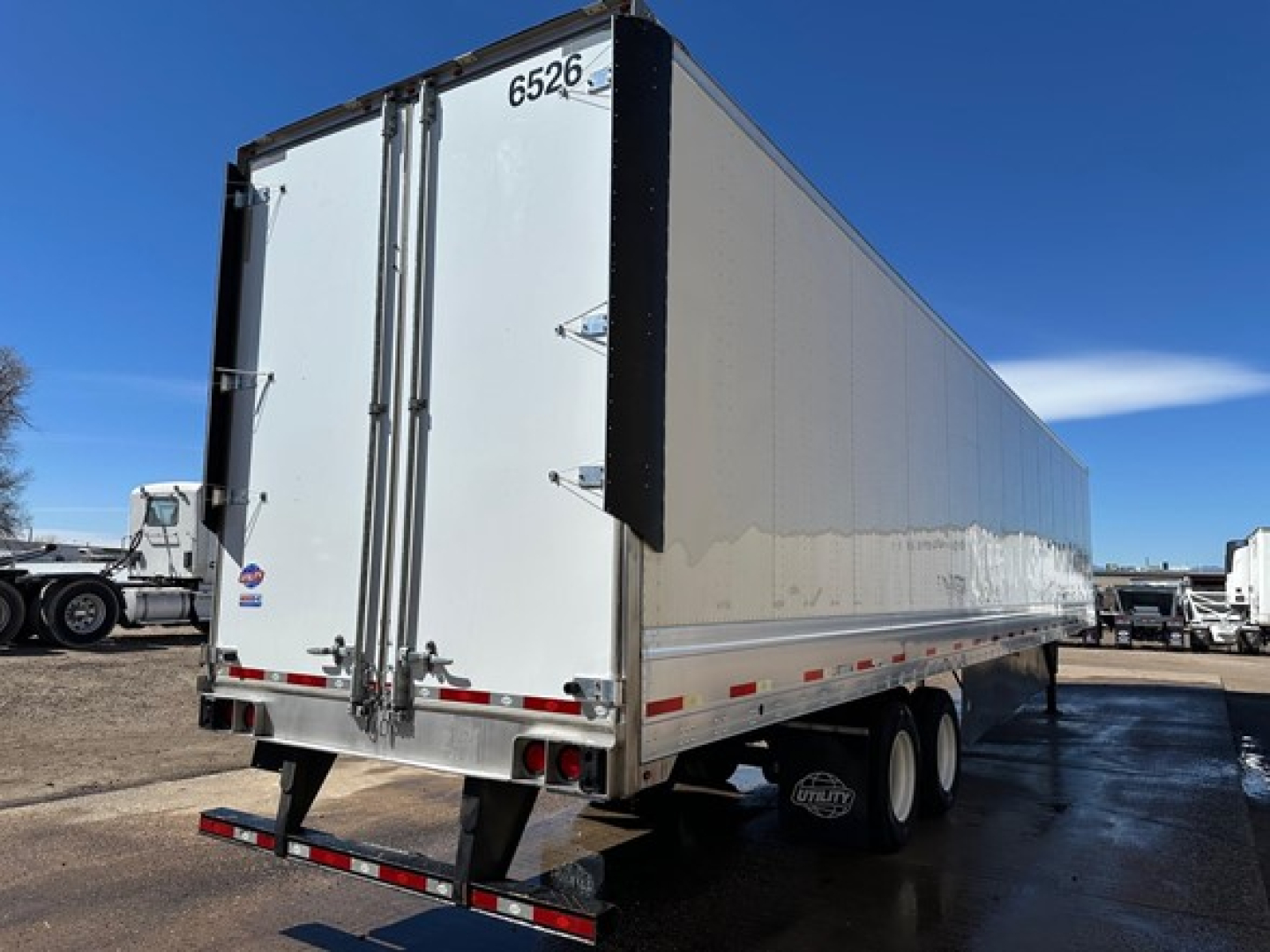Trailer side and rear showing a long aluminum box trailer with rear double doors and tandem wheels.