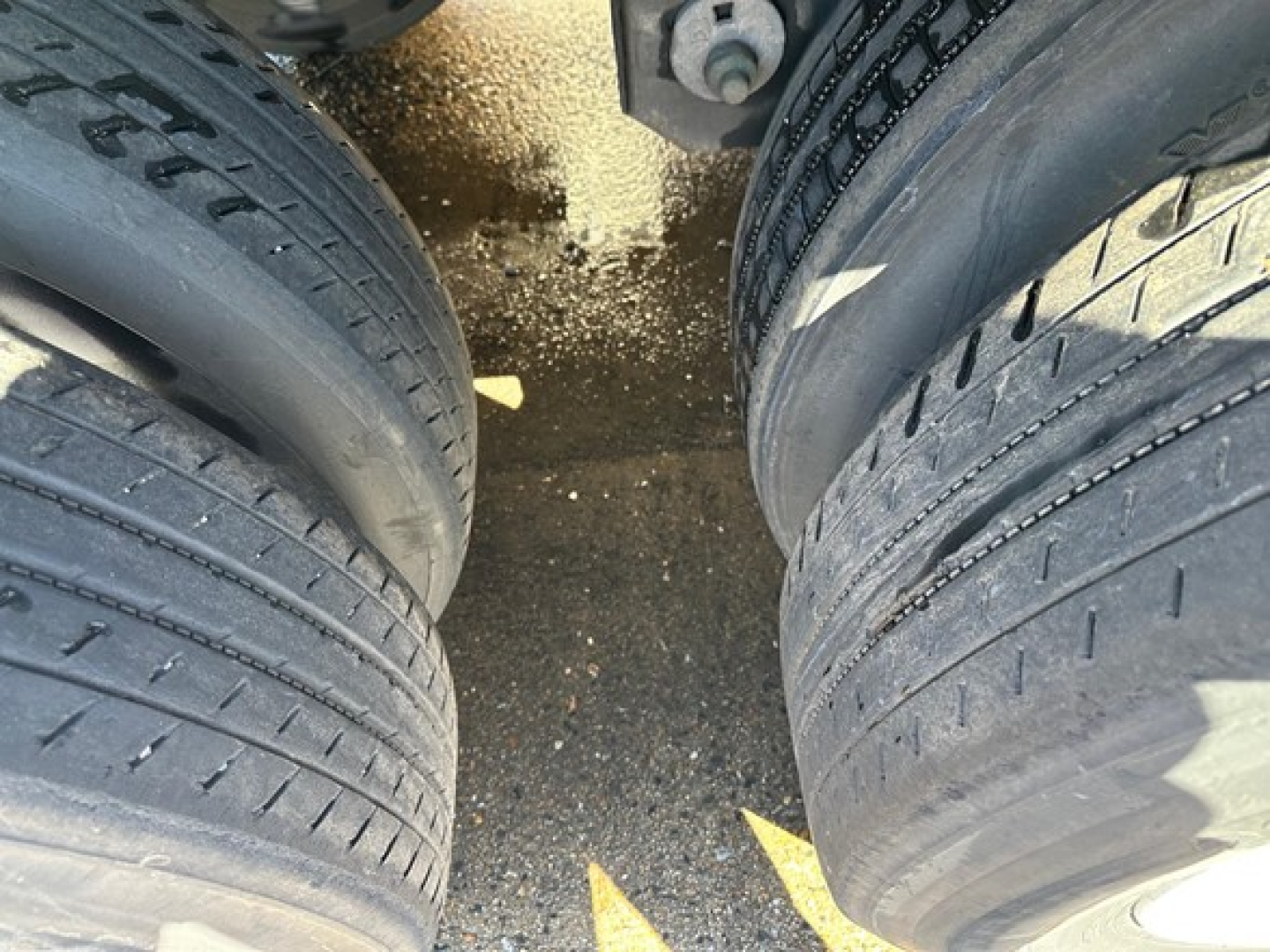 Two trailer tires with treads visible, undercarriage and side with a narrow gap, ground surface with specks.