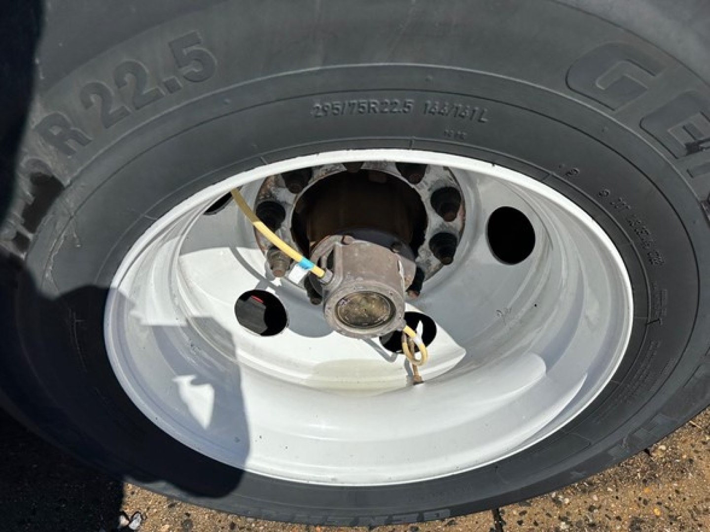 Truck trailer wheel assembly showing tire marked 295/75R22.5 and white steel rim with hub and brake components visible.
