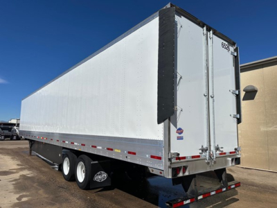 Trailer side and rear view showing a silver Utility 4000Dx box trailer with white side walls, dual rear doors, black corner guards, and tri-axle wheels.