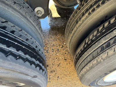Dual trailer tires mounted on a Utility trailer showing tread and wear, with gravel ground beneath.