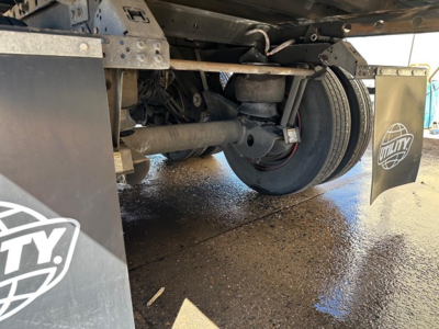 Trailer undercarriage showing axle, leaf springs, and tire assembly with Utility brand mudflap in view.