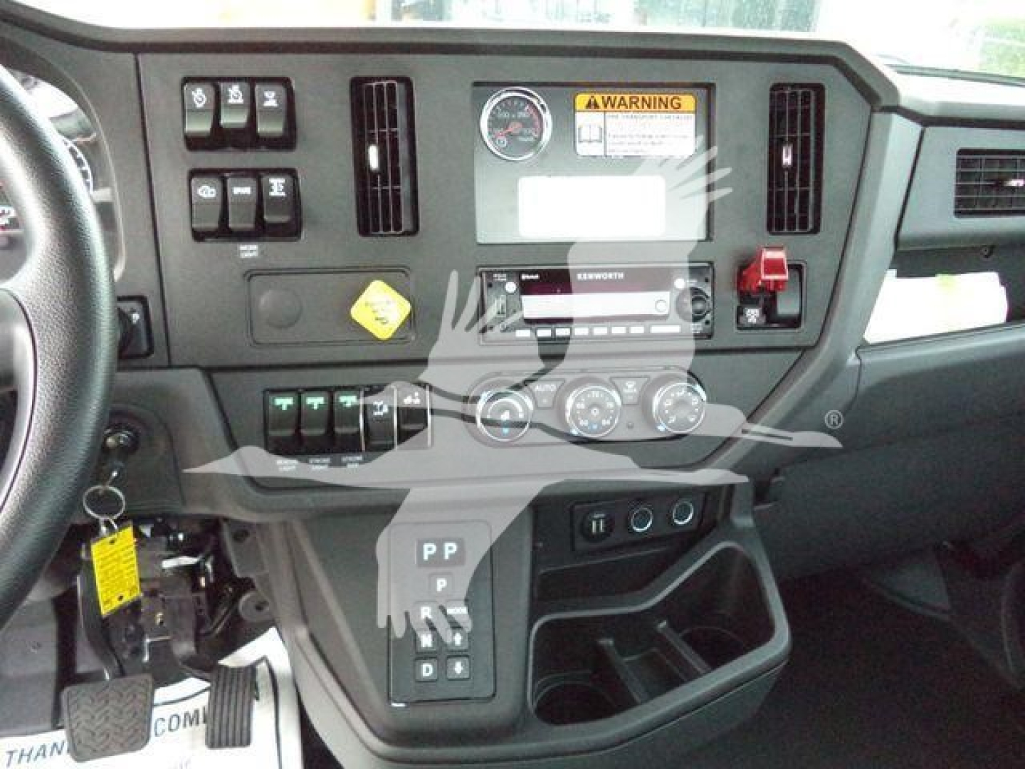 Dashboard view of a 2025 Kenworth T280 showing center console controls, gauges, and gear selector with labels.