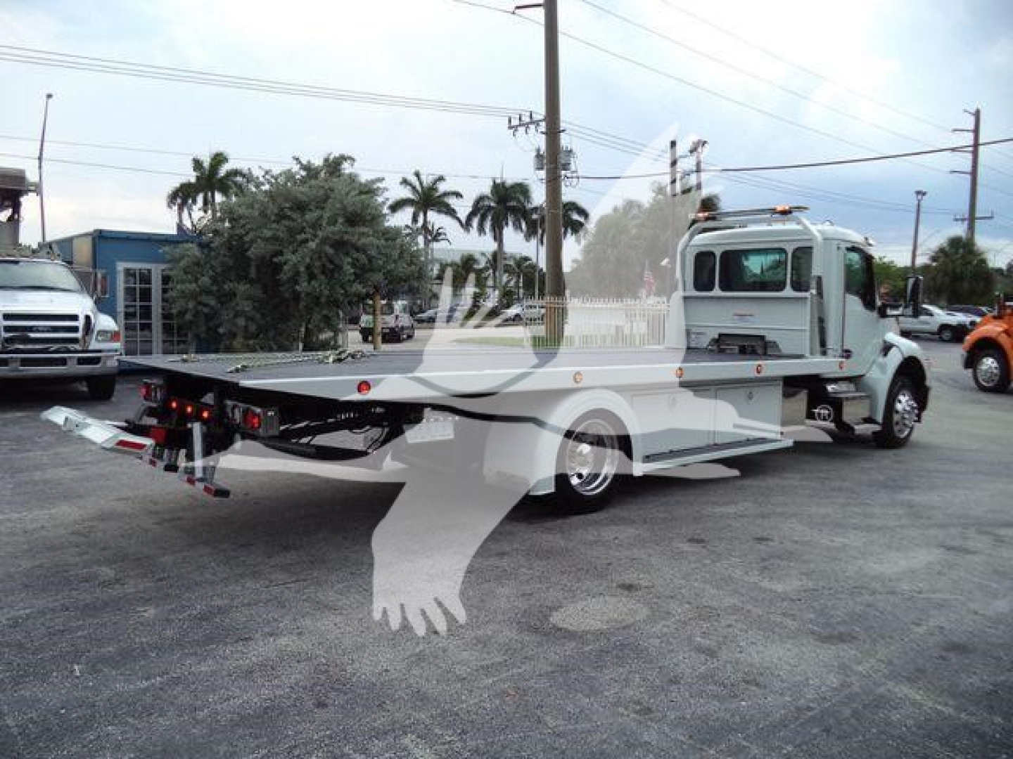 Kenworth T280 rollback tow truck side view showing flatbed with hydraulic cradle and truck cab in light color.