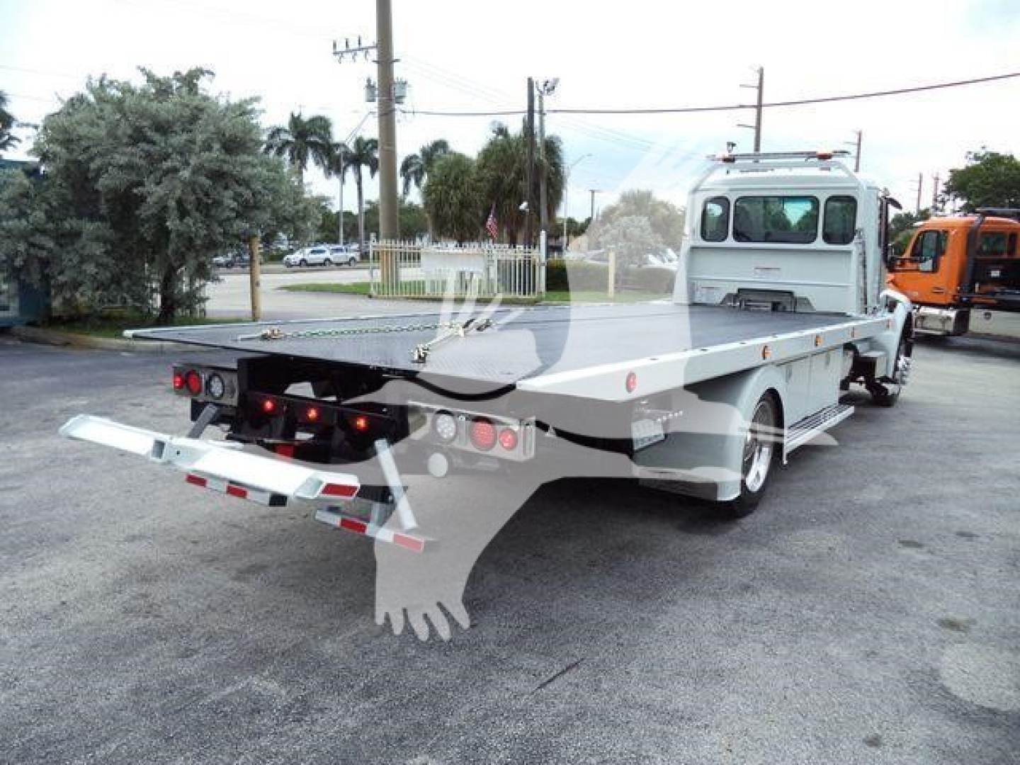 Kenworth rollback truck with flatbed and rear ramps; white color; side and rear view showing hitch and hydraulic equipment