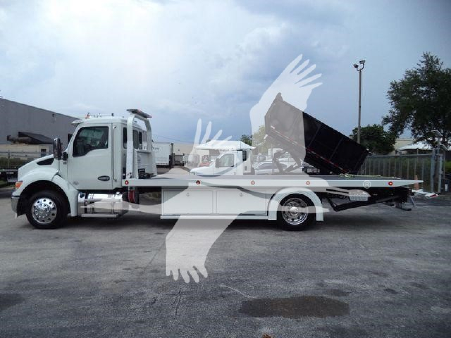 Kenworth T280 rollback tow truck in service view showing flatbed with hydraulic system and cab.
