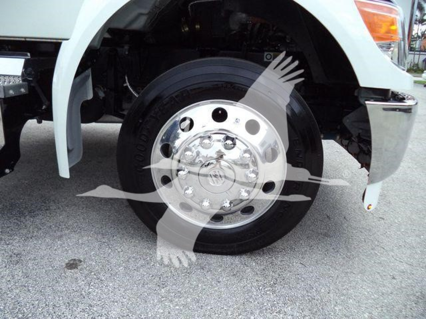 Kenworth T280 front wheel and fender showing front wheel hub with chrome lug nut cover and tire; partial bumper and white body panel visible.