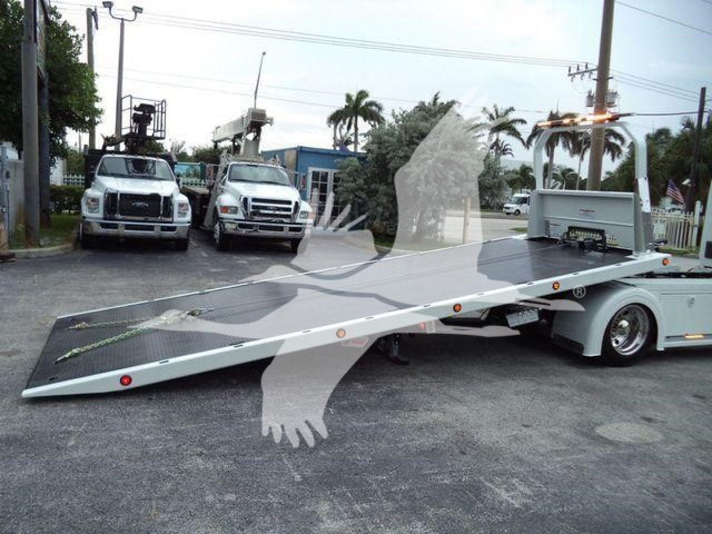 Kenworth T280 rollback tow truck with flatbed parked in a lot; two support trucks in background