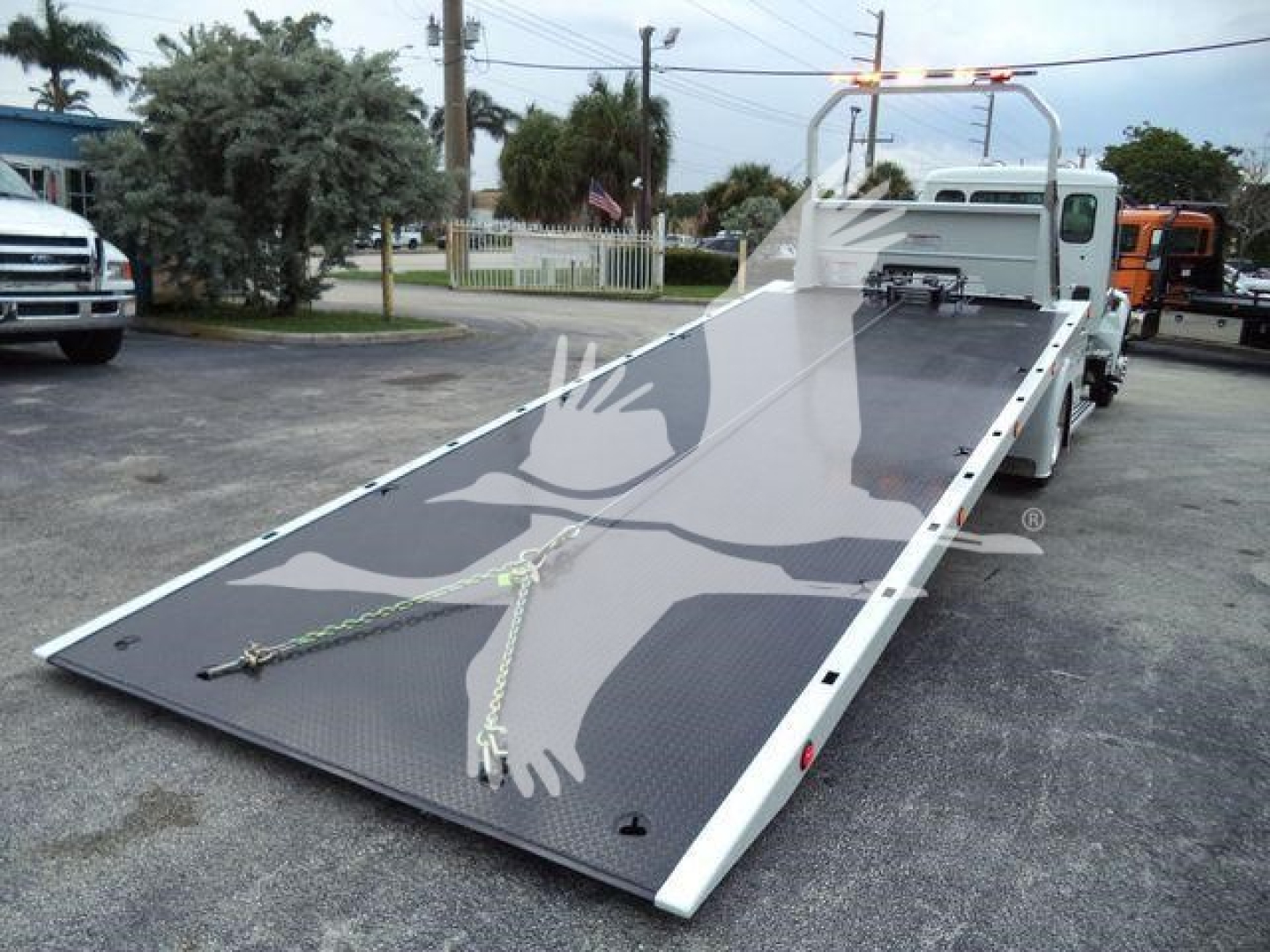 Kenworth T280 rollback truck with a raised flatbed ramp showing reflective surface and safety rails.