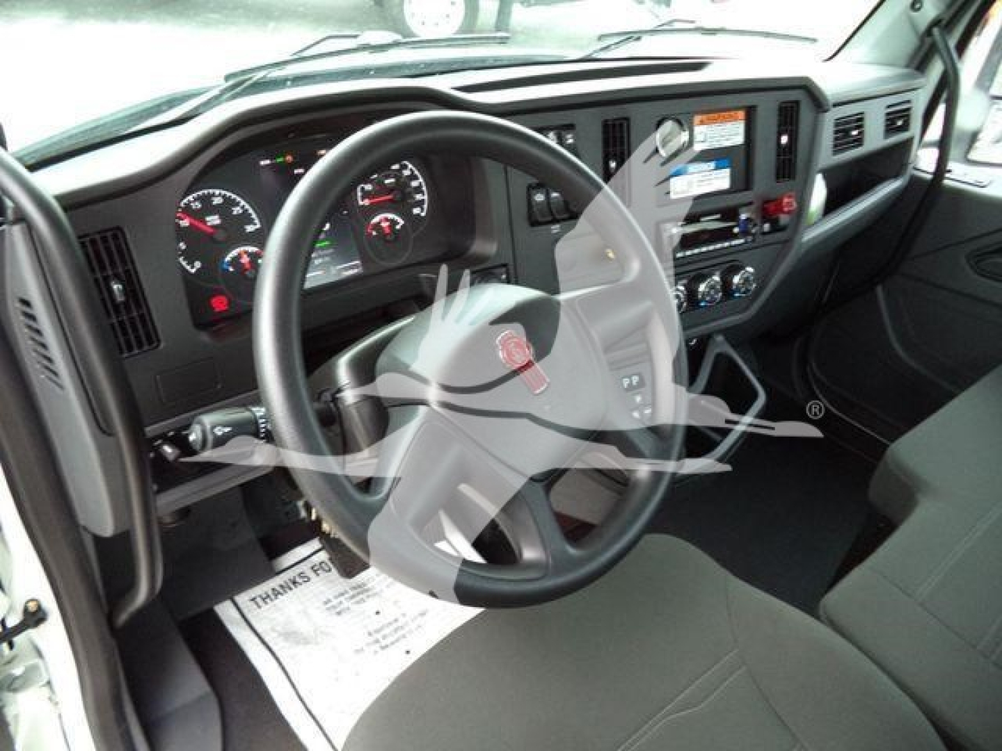 Dashboard and steering wheel of a Kenworth truck cab with instrument cluster, steering wheel emblem, and center console controls.