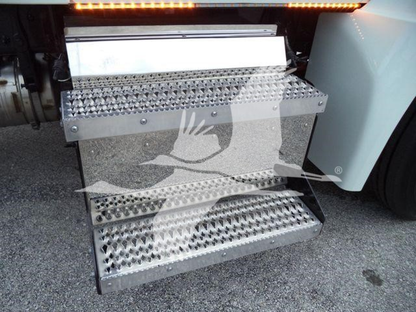 Kenworth truck stepside access step with perforated metal treads, undercarriage visible; white body panel on right.
