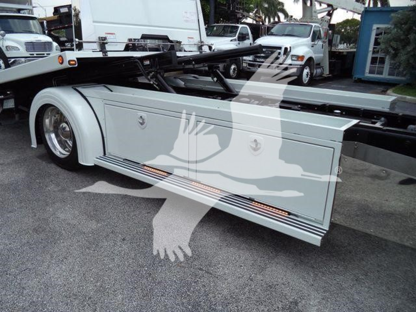 Kenworth T280 rollback truck side panel with storage box and steps visible, metallic silver color, logo emblems, and rear fender; stock image with other trucks in background.