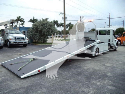 Kenworth T280 rollback tow truck with extended flatbed and rear wheel lift, white cab, gray bed, in a dealership lot.