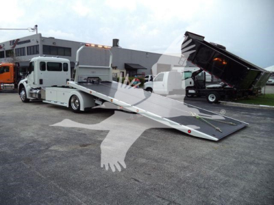Tow truck with a lowered flatbed and hydraulic rollback showing KW stock number in a truck lot.