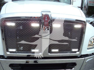 Truck front grille of a Kenworth T-series showing chrome grille with KW emblem and LED daytime running lights.