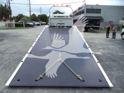 Kenworth T280 rollback truck platform in lowered position, measured hydra-lift surface with chains and towing hooks, front with white safety rail, dealership lot in background.