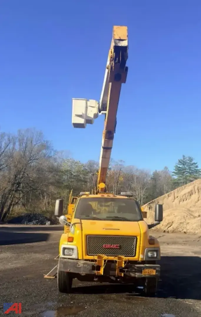 GMC TopKick C7500 utility truck on site with an extendable boom raised overhead, yellow cab, front grille, and stabilizers visible.
