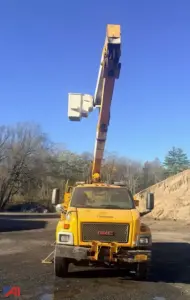 GMC TopKick C7500 utility truck on site with an extendable boom raised overhead, yellow cab, front grille, and stabilizers visible.