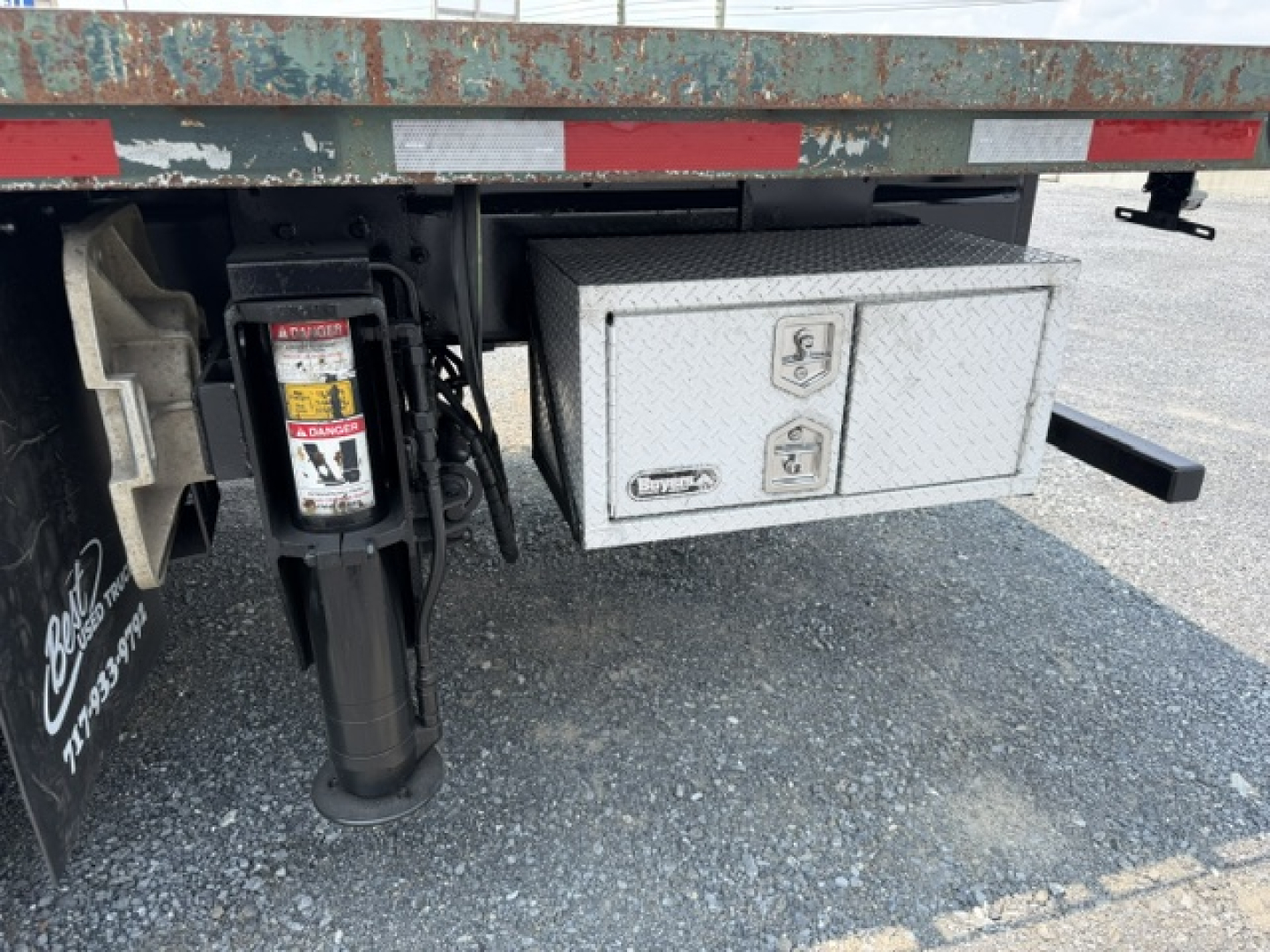 Truck rear showing hydraulic jack stand and metal toolbox with two latches on flatbed.