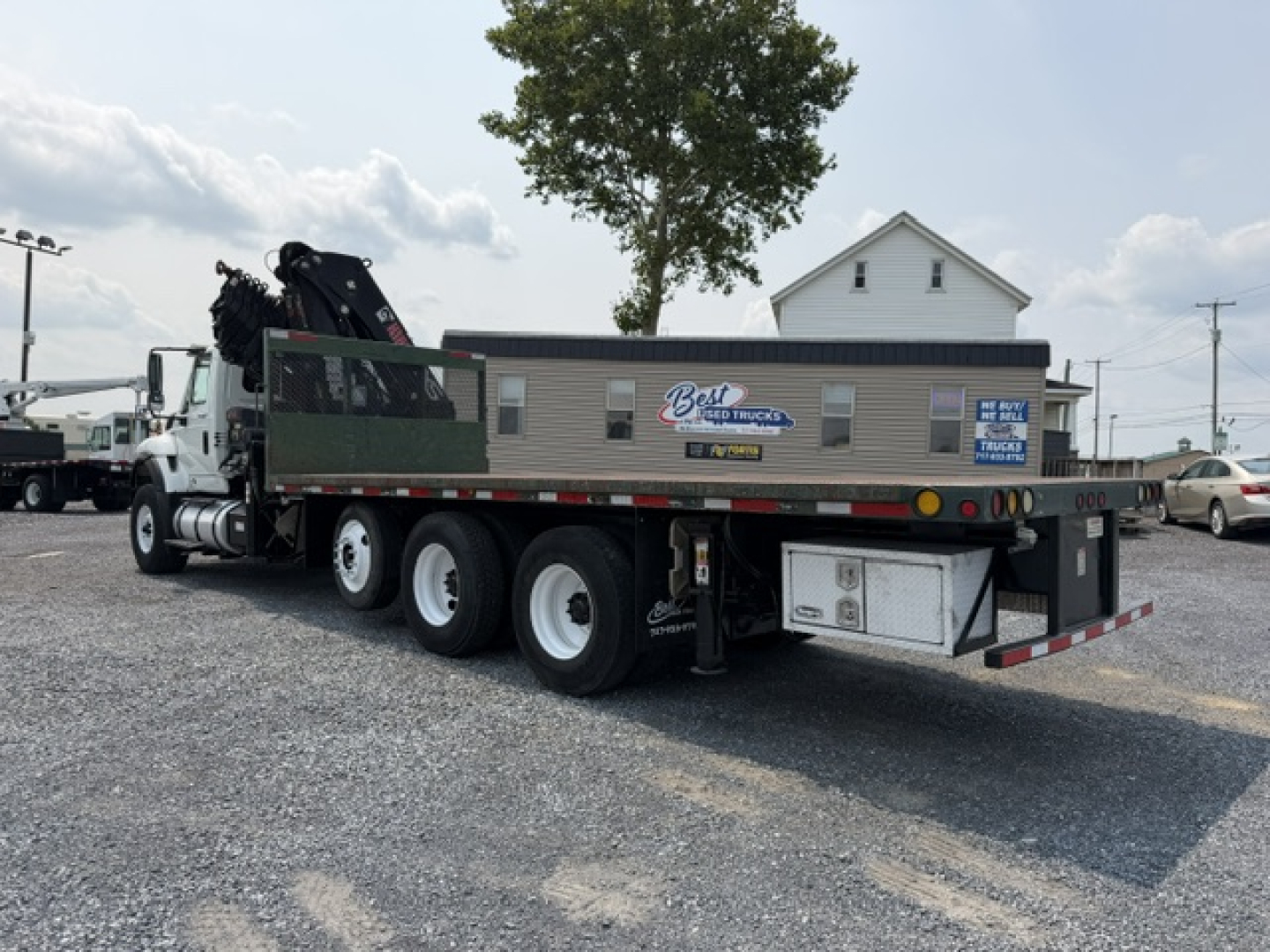 Truck crane flatbed with three rear axles and a mounted crane. Side panel shows Blaine? sticker and some text. License plate area near rear. Overall shows tool storage boxes and bumper.