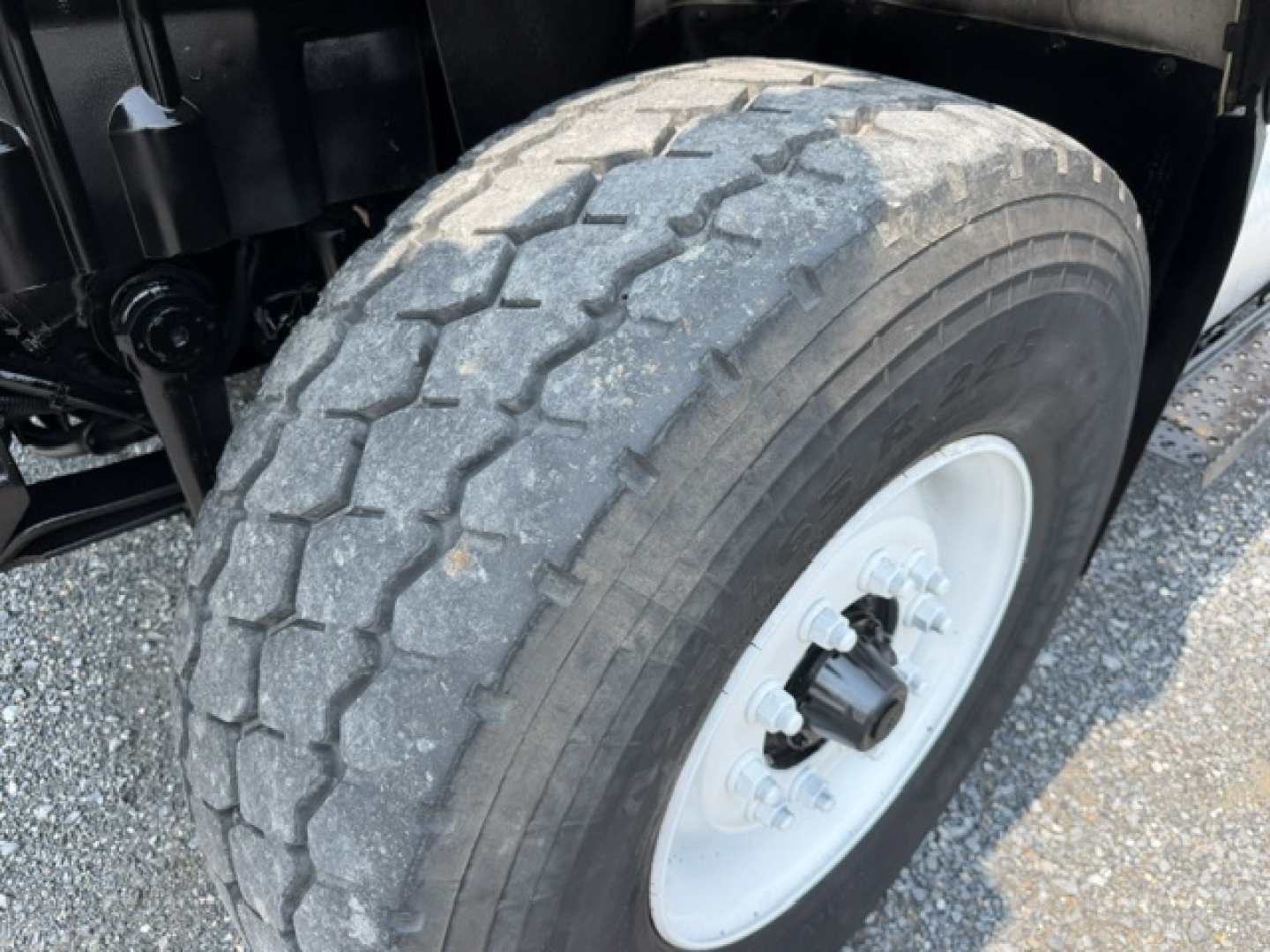 Truck front wheel well and tire with tread pattern, white steel wheel, visible suspension components