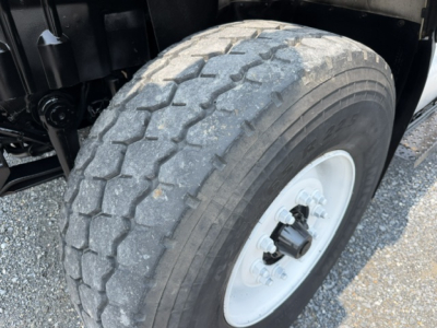 Truck front wheel well and tire with tread pattern, white steel wheel, visible suspension components