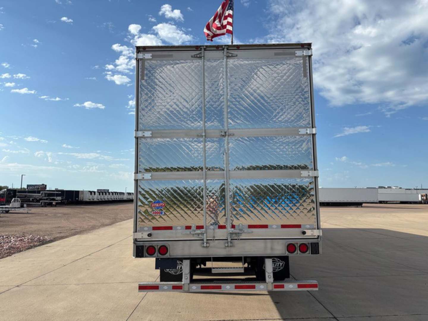 Rear view of a new 2027 utility refrigerated trailer with diamond plate metal doors, rear lights, and a small American flag on top.