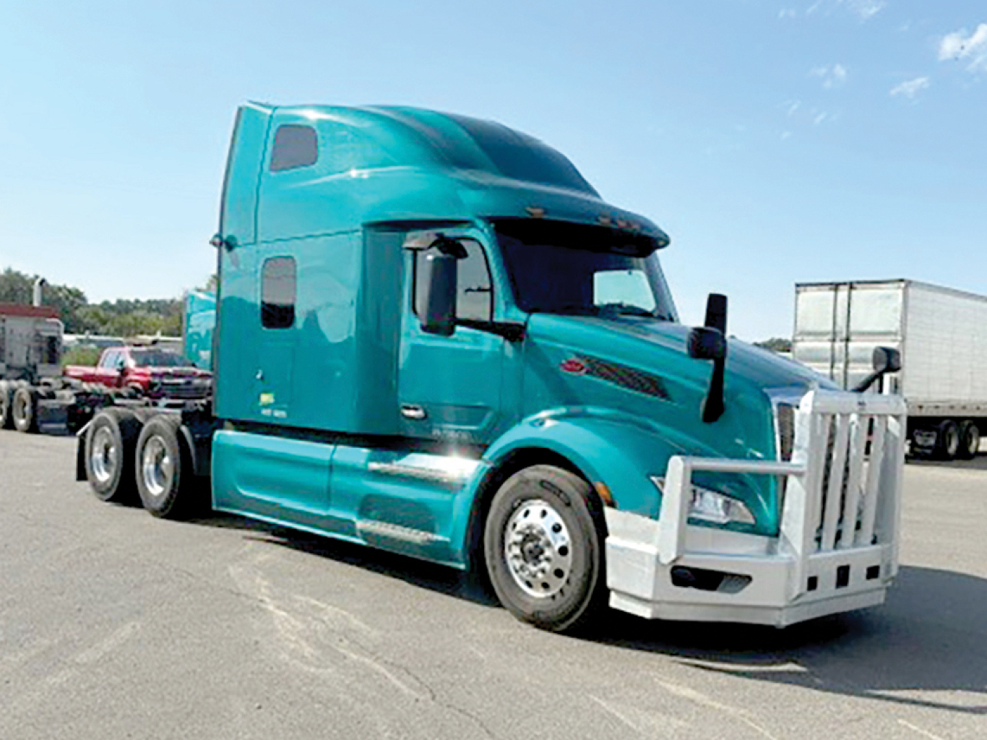 Peterbilt 579 axle truck in teal with large grille guard, side mirrors, and sleeper cab.