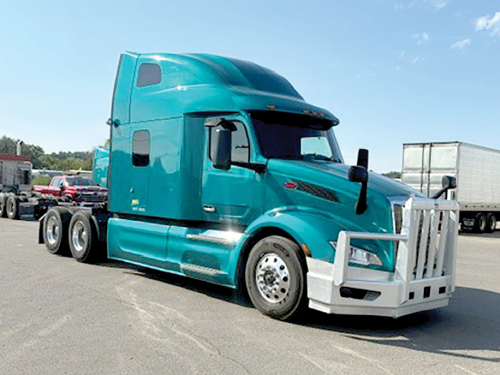 Peterbilt 579 axle truck in teal with large grille guard, side mirrors, and sleeper cab.