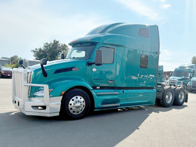 Peterbilt 579 semi-truck in teal color, front quarter view showing sleeper cab, chrome bumper, and dual rear axles.