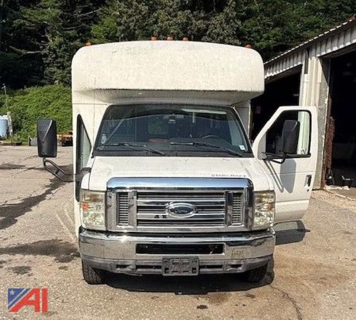 Front view of a white 2011 Ford E350 mini bus with wheelchair lift, front doors open, chrome grille, bus body, in a lot.