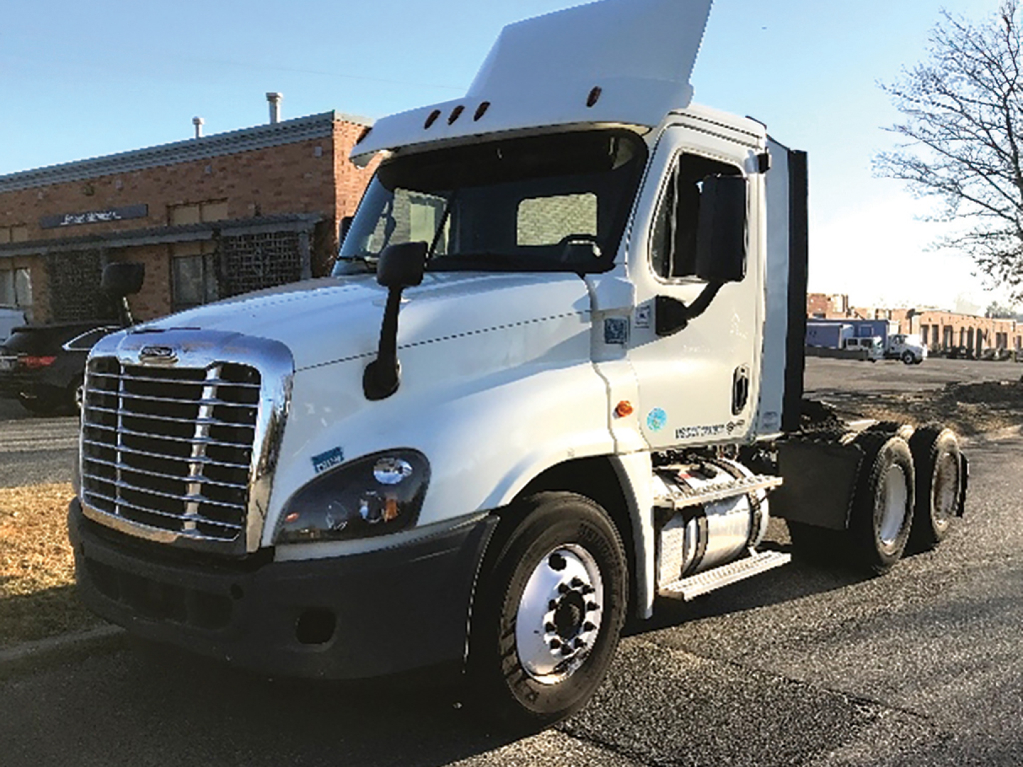 Truck cab with silvery white Freightliner Cascadia 125 daycab, front grille, fuel tanks, and dual rear axles visible.