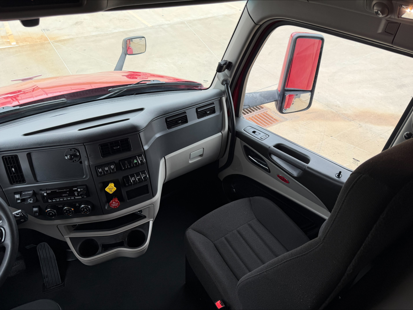 Truck cab interior of a 2023 Peterbilt 579 showing the driver's seat, steering wheel, dashboard, and door panel with controls.
