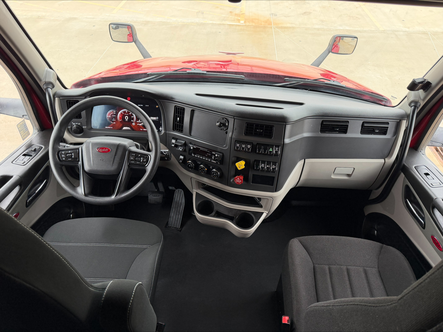 Truck cab interior of a 2023 Peterbilt 579 from the driver seat perspective, showing steering wheel, dashboard with gauges, center console, and driver and passenger seats.