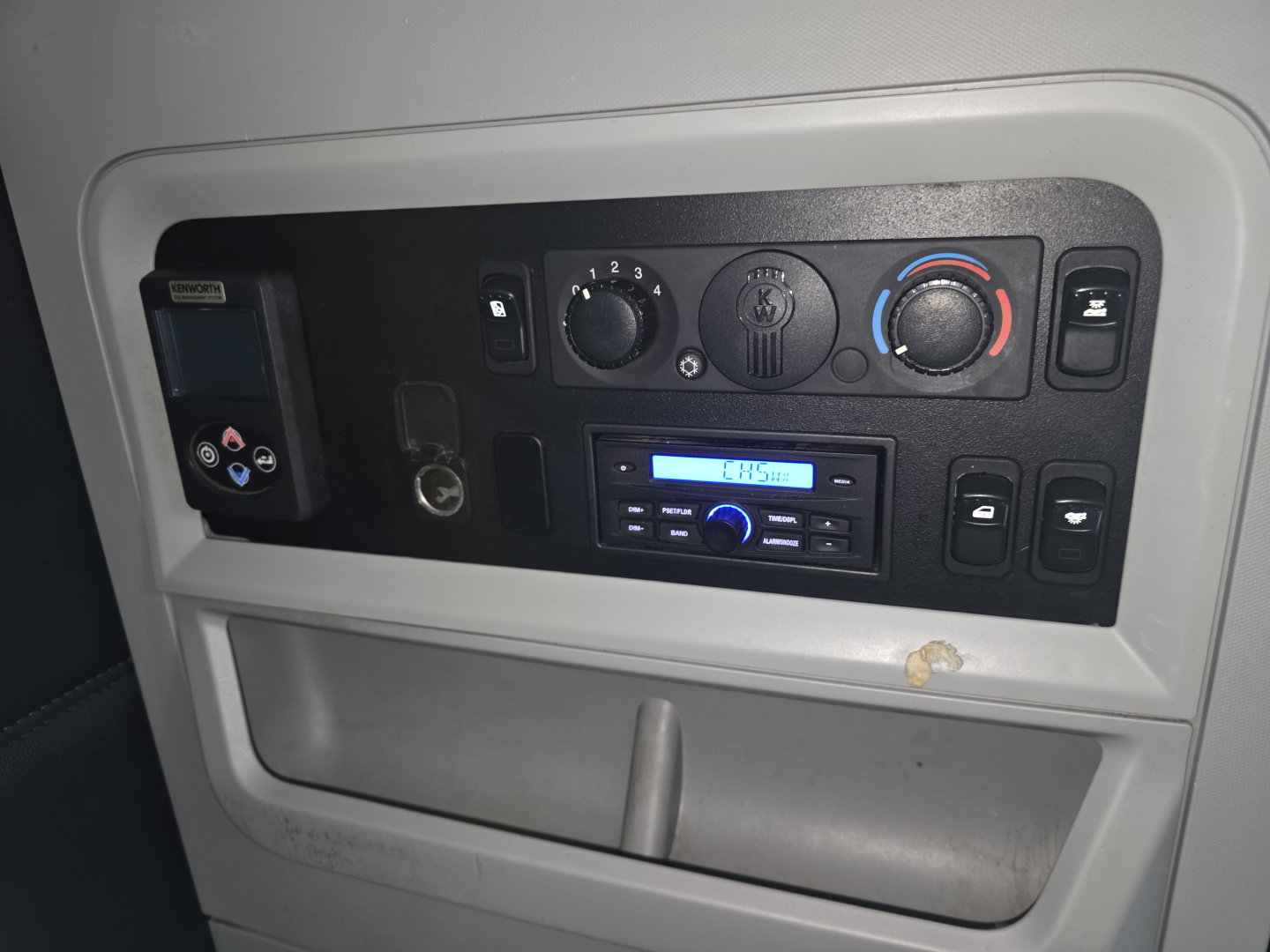 Cabin control panel and HVAC knobs in a Kenworth T680 truck, showing climate controls, radio, and storage area.