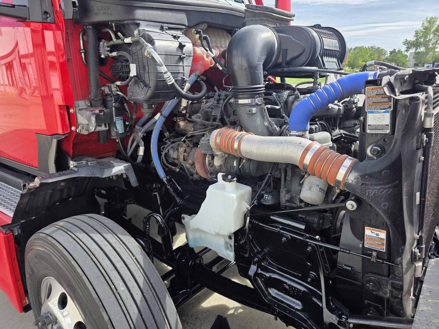 Kenworth T680 engine bay view showing coolant reservoir and various hoses and blue silicone hose on right side.