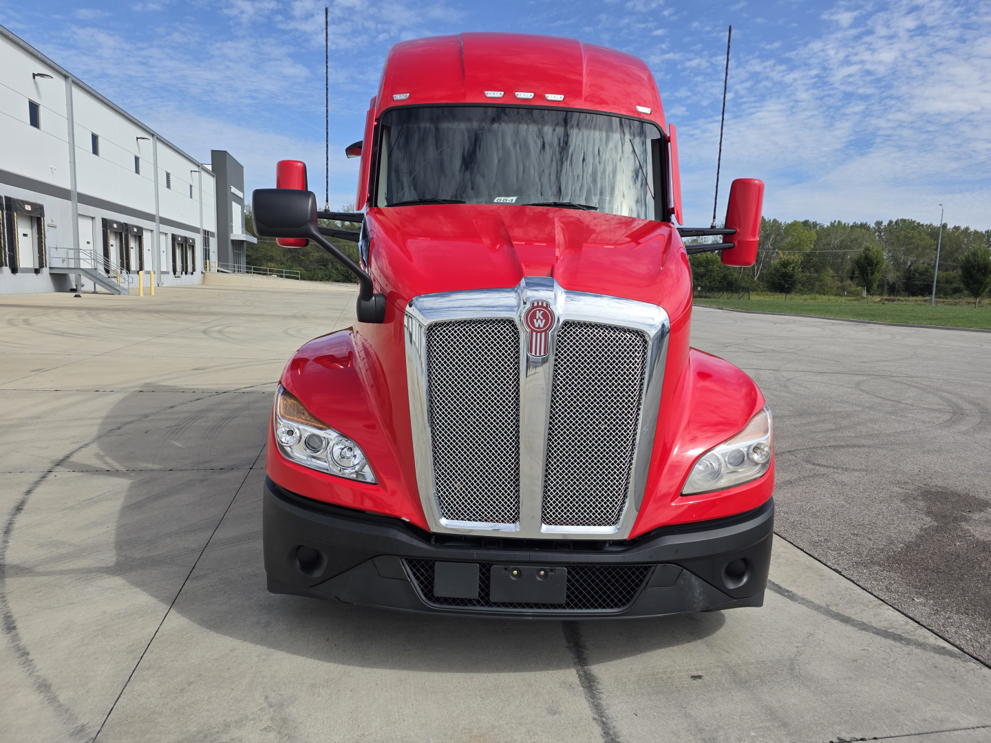 Red Kenworth T680 truck front view showing chrome grille, headlights, and large mirrors.