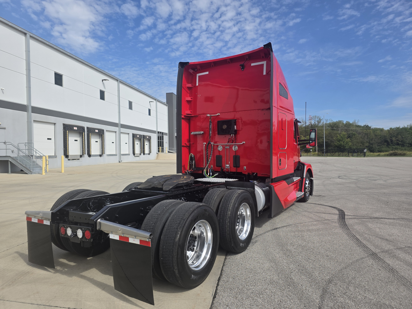 Kenworth T680 tractor rear view showing red sleeper cab and dual rear axles in a parking lot.