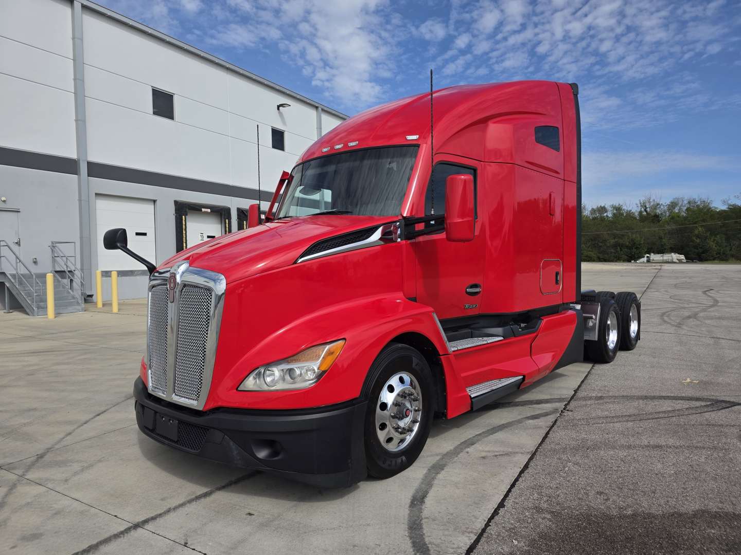Kenworth T680 sleeper cab truck in red, front left view, with dual rear axles and chrome grille, parked in lot.