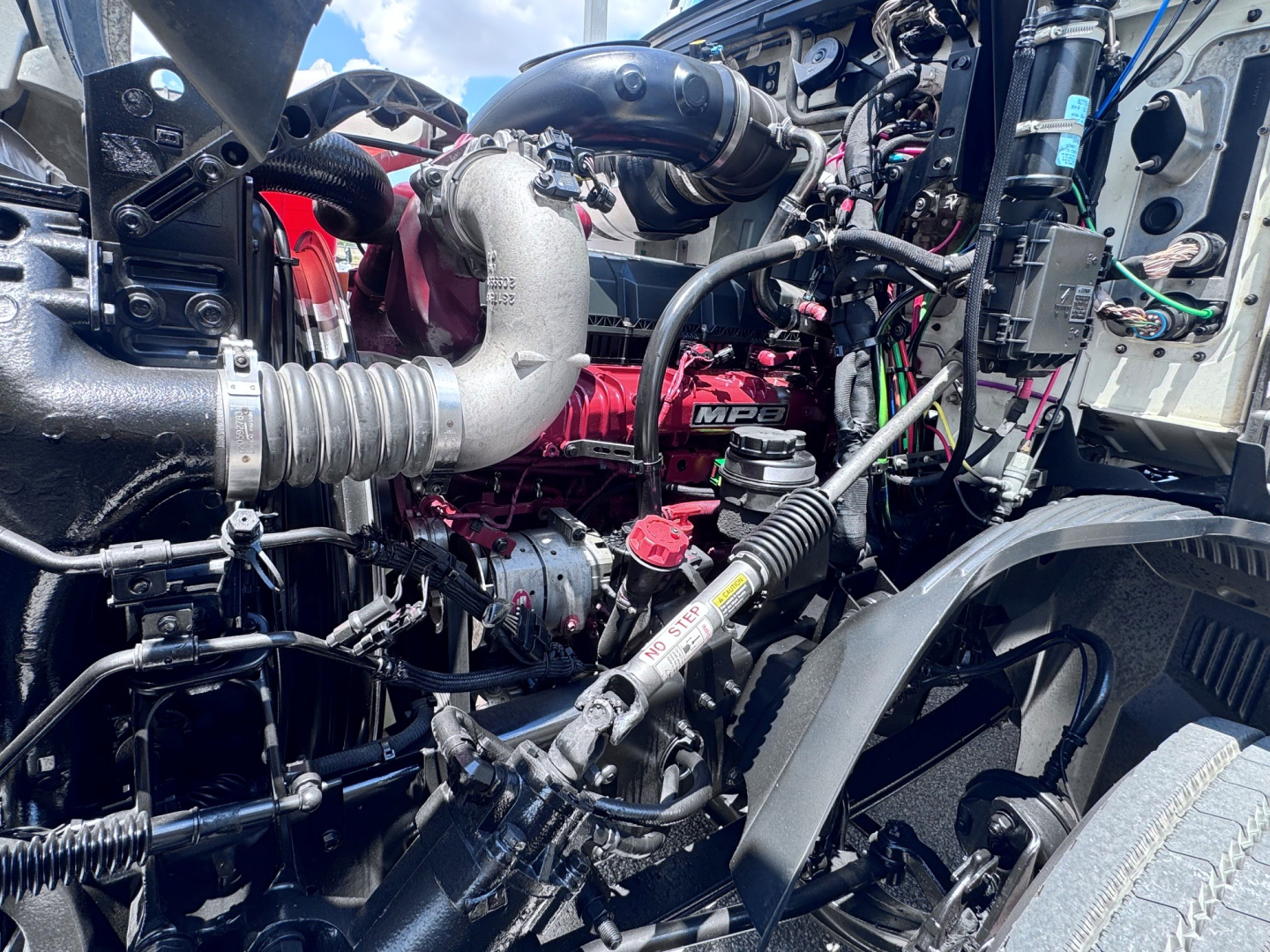 Truck engine bay showing turbocharged engine with intercooler piping, hoses, wiring, and air intake near front wheel well.