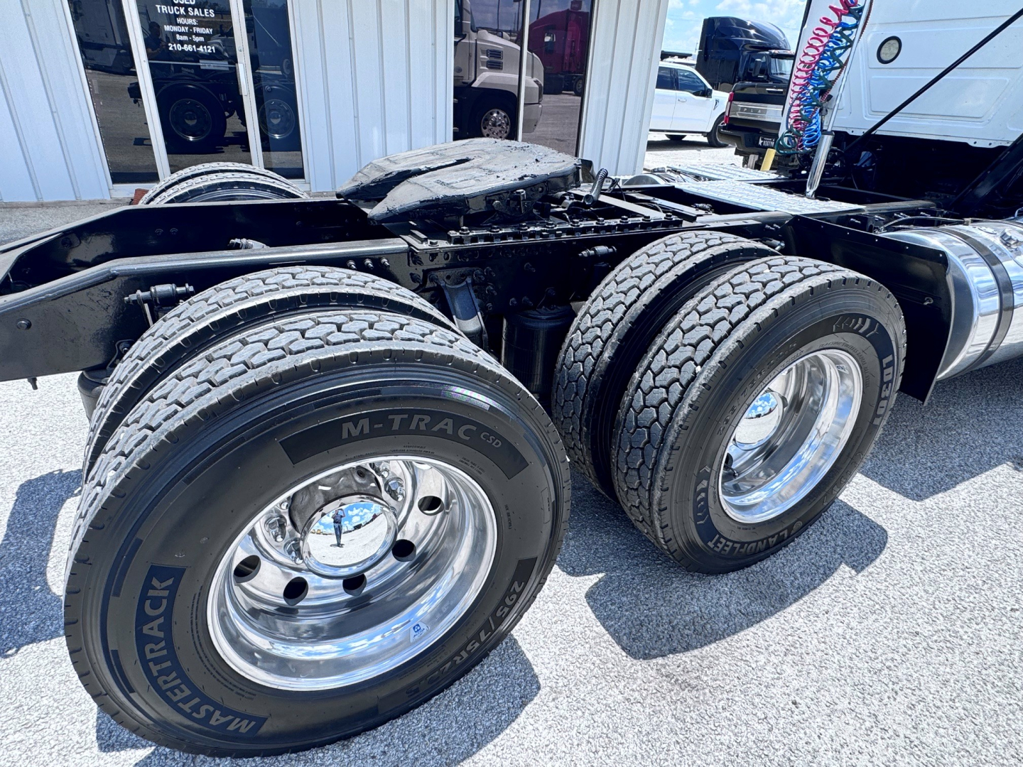 Mack ANTHEM truck chassis showing dual rear axles with M-TRAC tires, chrome wheels, and adjacent fuel tank; visible tire sidewall reads 'MIR...'. The frame is exposed with suspension and rear wheels.
