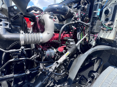 Truck engine bay showing turbocharged engine with intercooler piping, hoses, wiring, and air intake near front wheel well.
