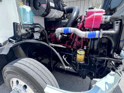 Engine bay of a 2020 Mack Anthem showing coolant reservoir, air intake, pink coolant reservoir, blue silicone hoses, yellow oil filter, and exposed engine components.