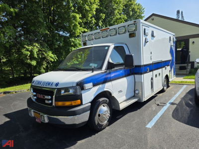 GMC Savana ambulance front-left view with blue and white livery, multiple rooftop medical compartments, and ‘AMBULANCE’ text on the cab grille area.