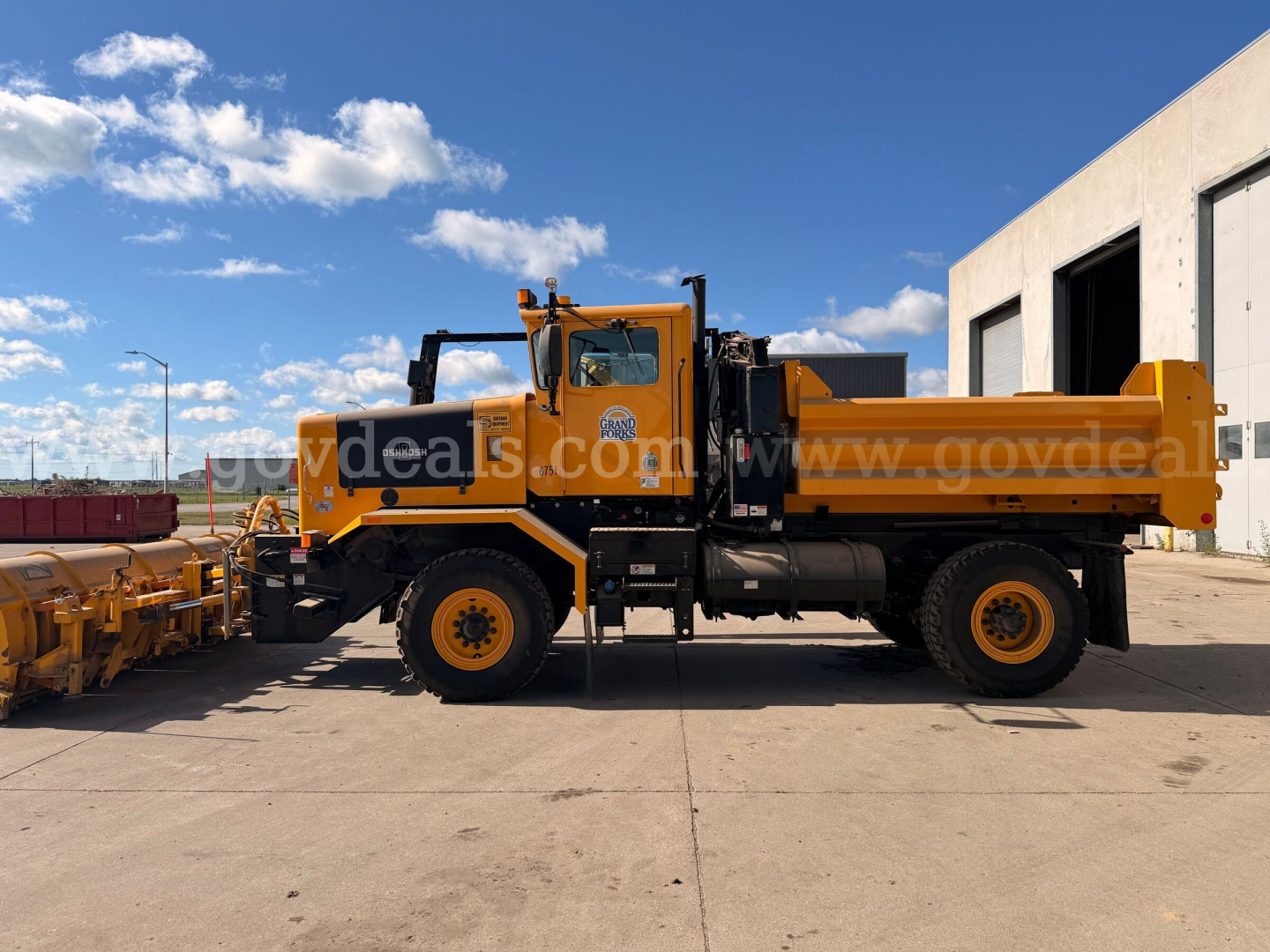 Orange Oshkosh forward-control truck with plow/loader attachment and dump bed, side view.